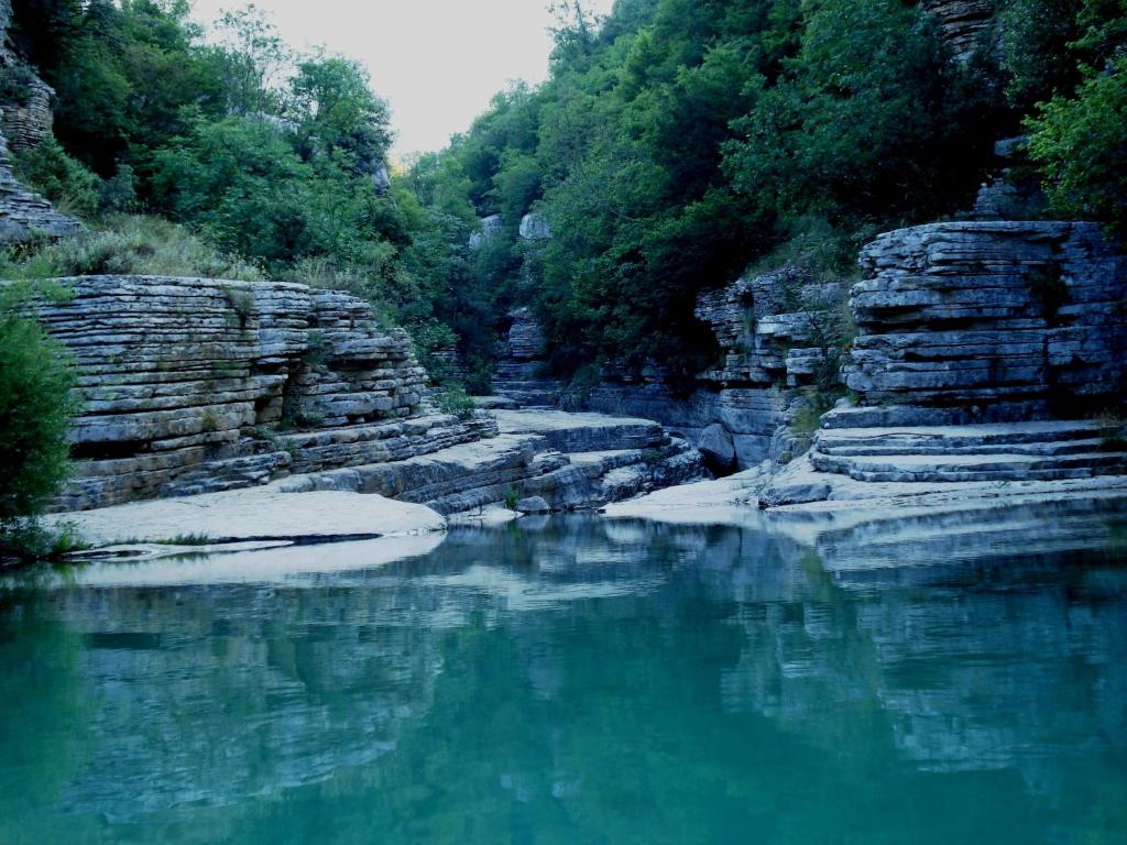 un fiume con acqua blu, rocce e alberi di Traditional Rooms karaouli a Papigko