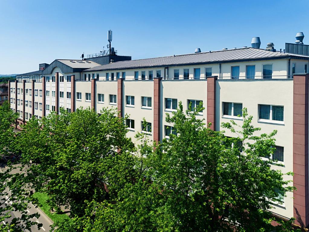 ein weißes Gebäude mit Bäumen davor in der Unterkunft Victor's Residenz-Hotel Saarlouis in Saarlouis