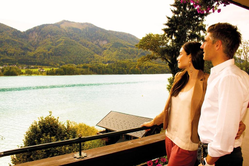 a man and a woman standing next to a lake at Hotel Seewinkel in Fuschl am See