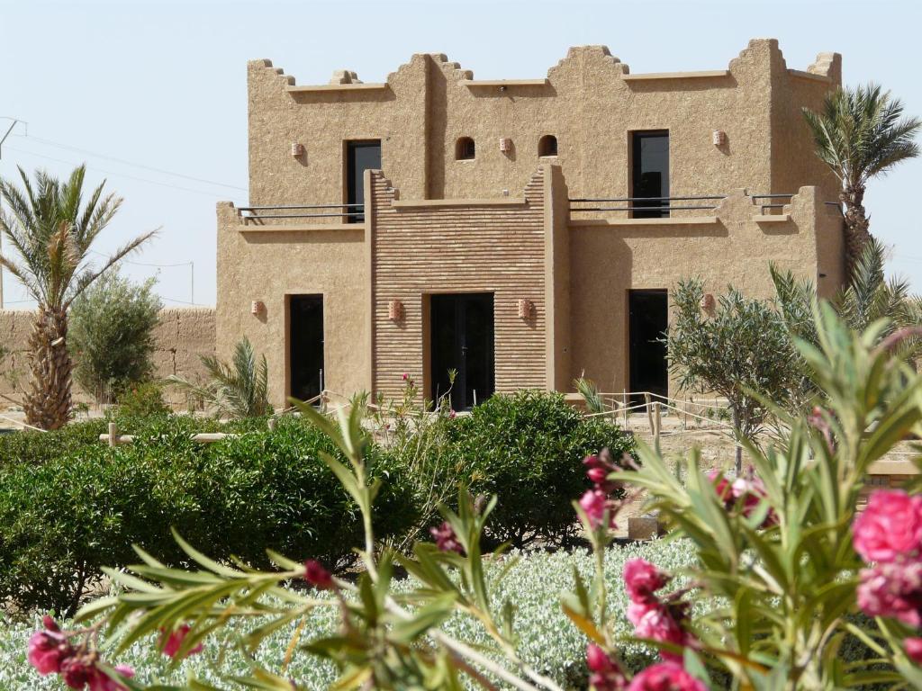 a building in the desert with flowers in the foreground at Tifina Caravanserail d'Arfoud in Erfoud