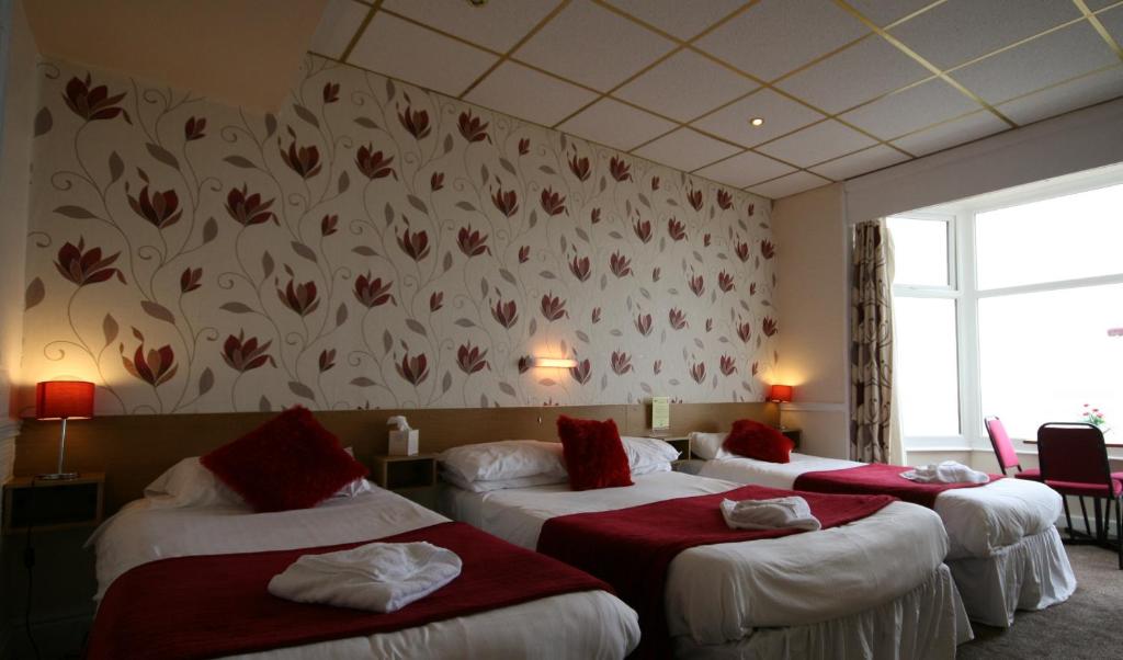 una camera d'albergo con tre letti con lenzuola rosse di The Blenheim Mount Hotel a Blackpool