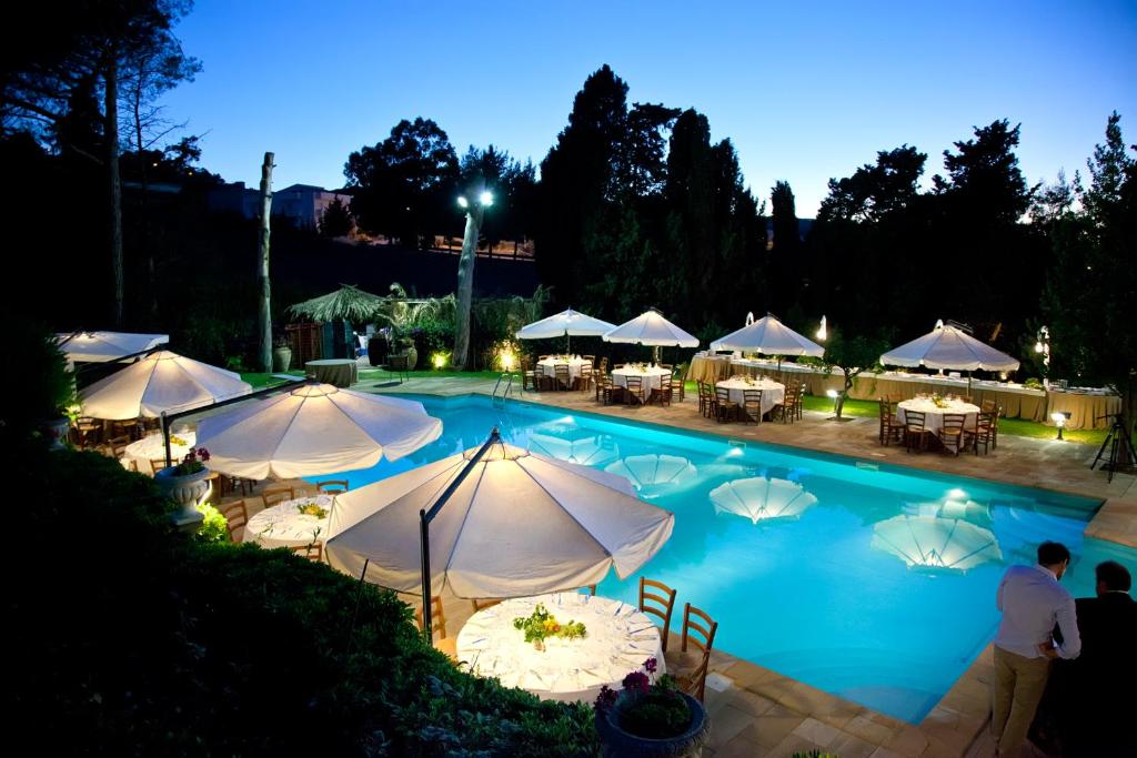 a swimming pool with tables and umbrellas at night at Agriturismo Baglio Fontana in Buseto Palizzolo