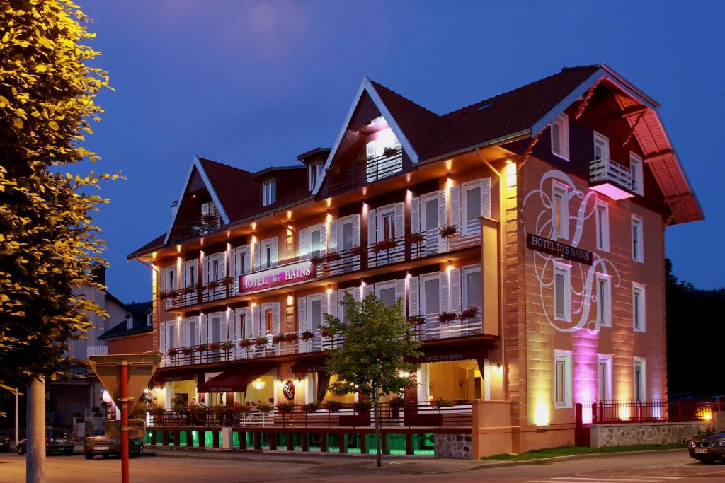 un grand bâtiment avec des lumières sur son côté dans l'établissement Logis Hotel Des Bains, à Gérardmer