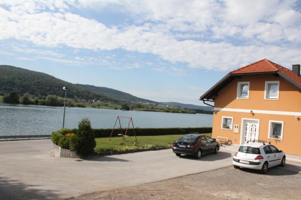 a house with two cars parked in front of a lake at Apartment Mihalic in Ogulin