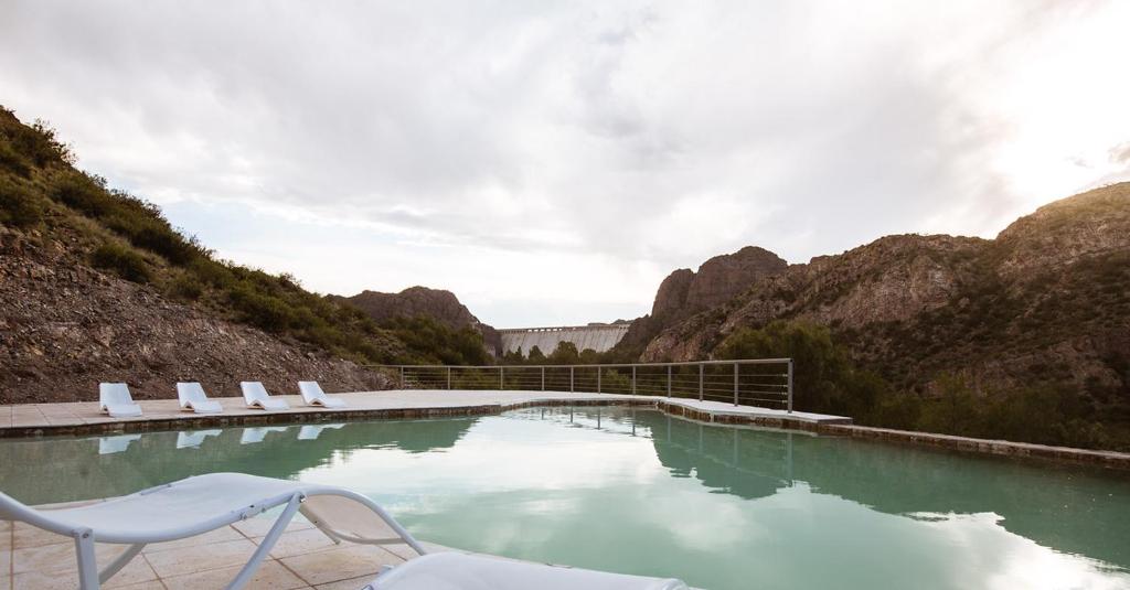 a pool of water with lounge chairs and mountains at Bosque Divino Cabañas & Suites in Valle Grande