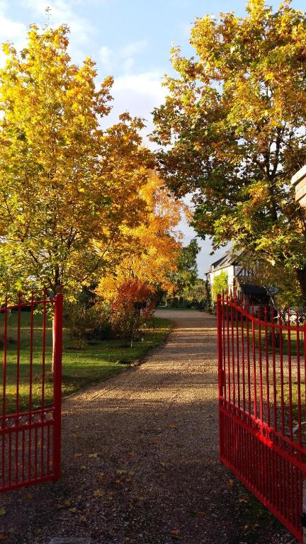 une clôture rouge devant une route arborée dans l'établissement Chambre d'hôtes - Le jardin des Patissons, à La Foret Du Parc