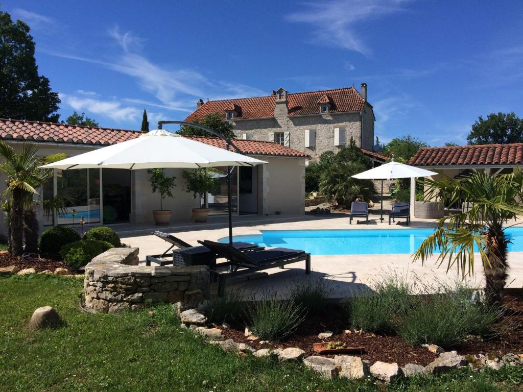 a swimming pool with two umbrellas and a house at Le Couvent in Saint-Jean-de Laurs
