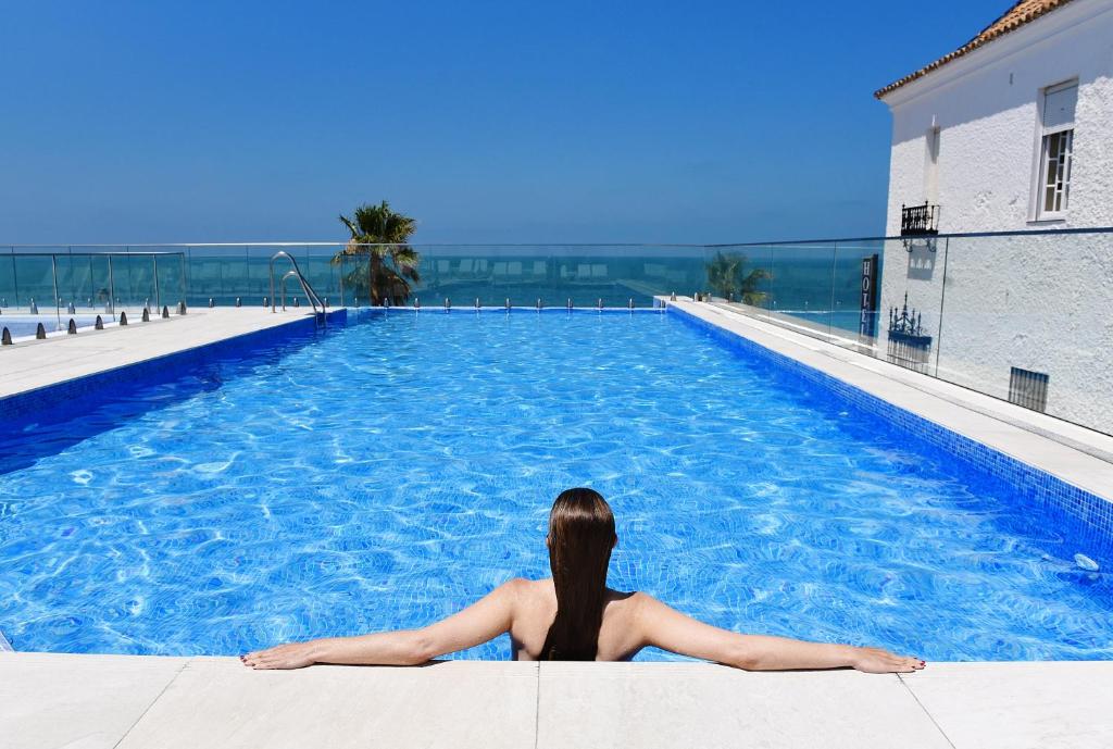 una mujer sentada en el borde de una piscina en Hotel Agaró, en Chipiona