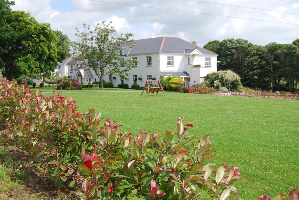 a white house with a large lawn and trees at Beggars Reach Hotel in Pembroke Dock