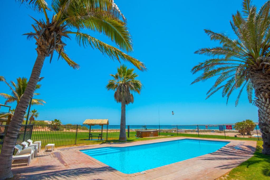 a swimming pool with palm trees and the ocean at Ningaloo Reef Resort in Coral Bay