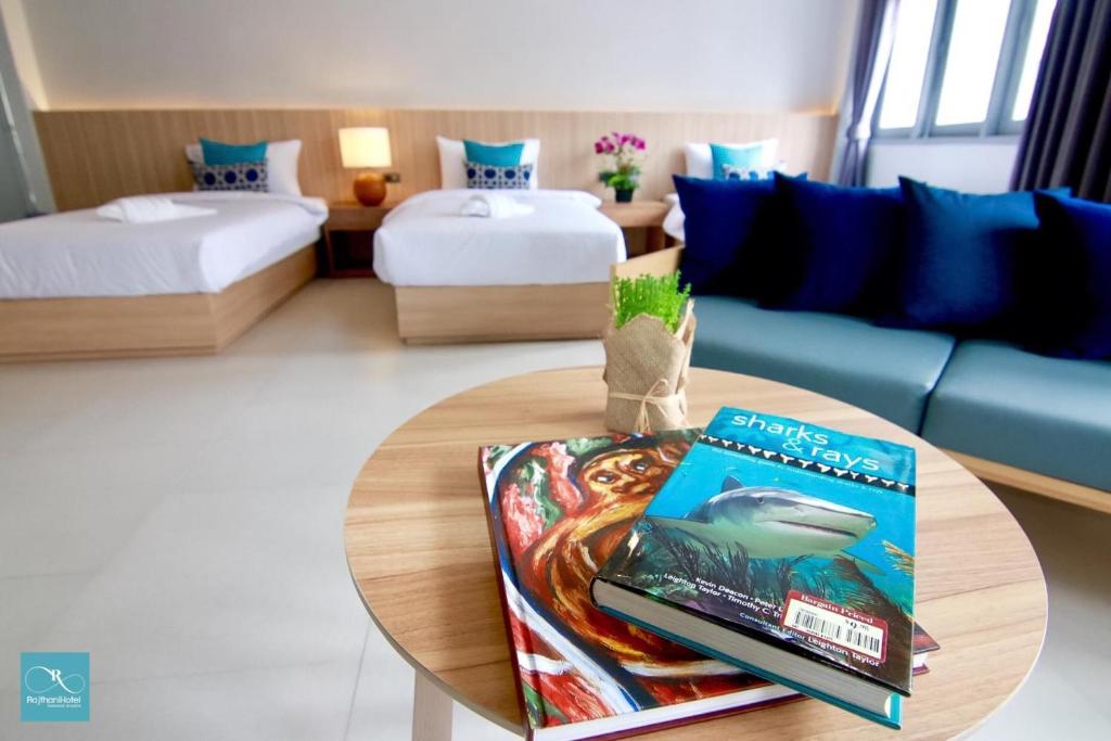 a room with two beds and a table with a book at Rajthani Hotel - SHA Certified in Surat Thani