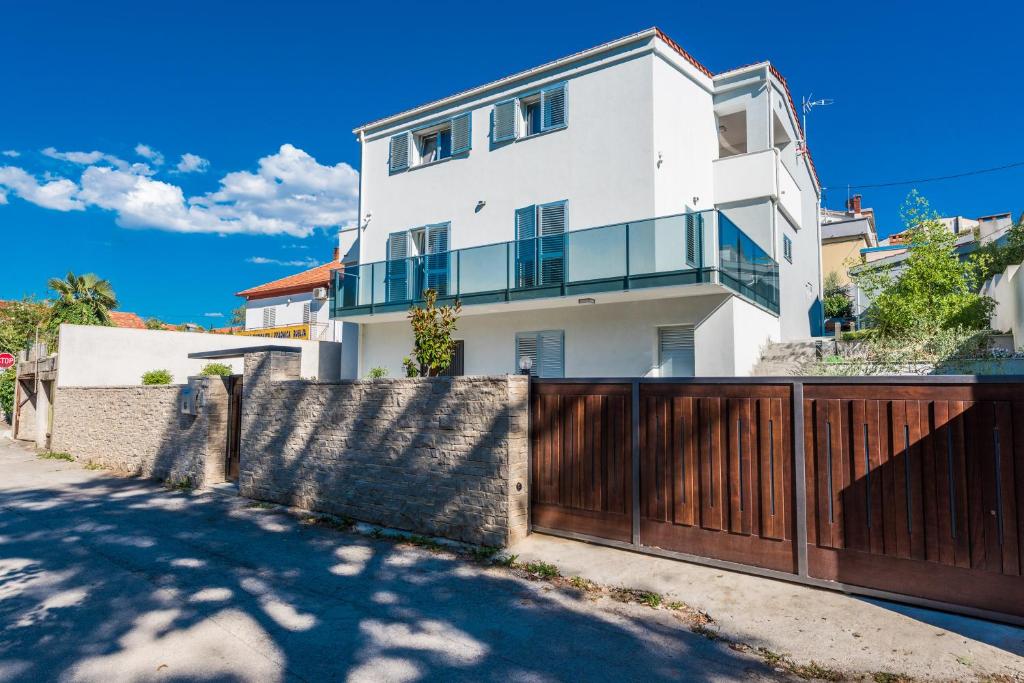 a white house with a wooden fence in front of a driveway at Apartments Ena in Zadar