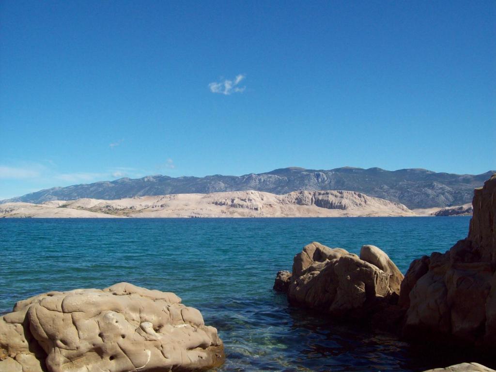 een grote rots in het water met bergen op de achtergrond bij Apartmani Vesna in Pag