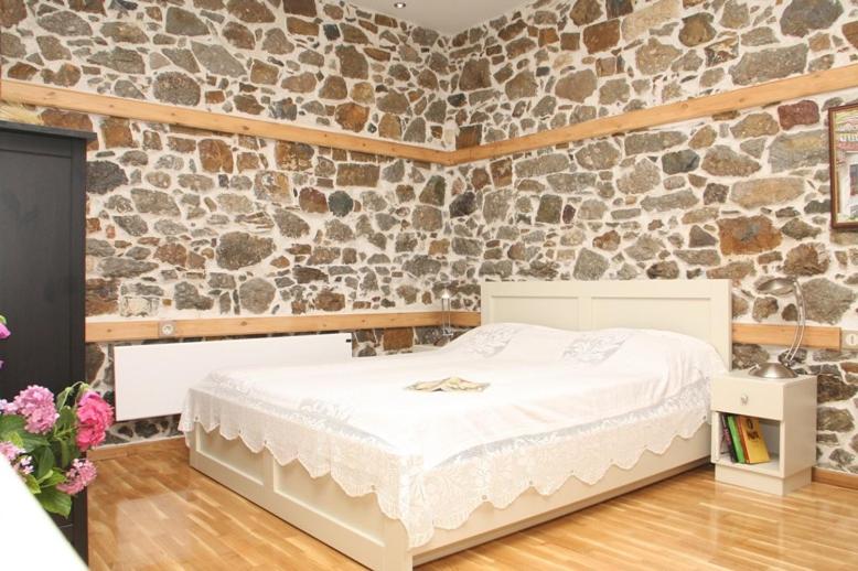 a bedroom with a white bed and a stone wall at Traditional Houses Atzanou in Samothráki