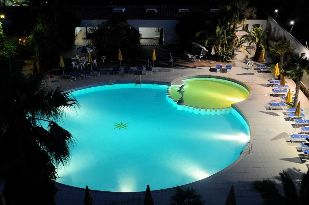 uma grande piscina à noite com cadeiras e uma praia em Marina Club Hotel em Baia Domizia