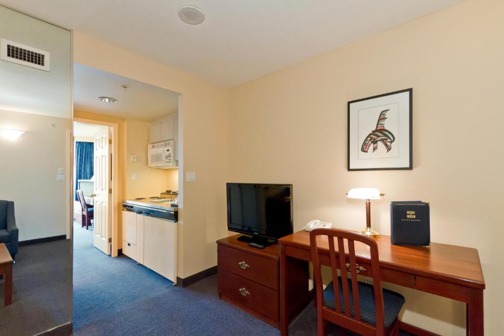 a room with a desk with a television and a kitchen at Rosedale on Robson Suite Hotel in Vancouver