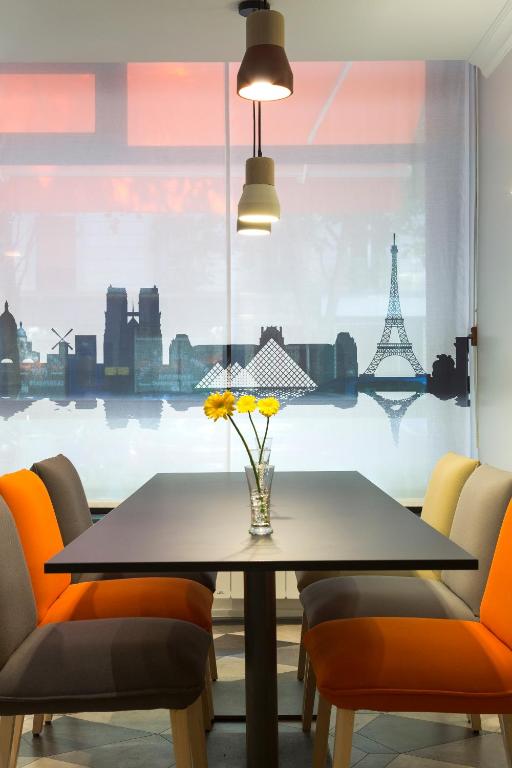 a dining table with orange chairs and a window with the eiffel tower at Citadines Bastille Gare de Lyon Paris in Paris