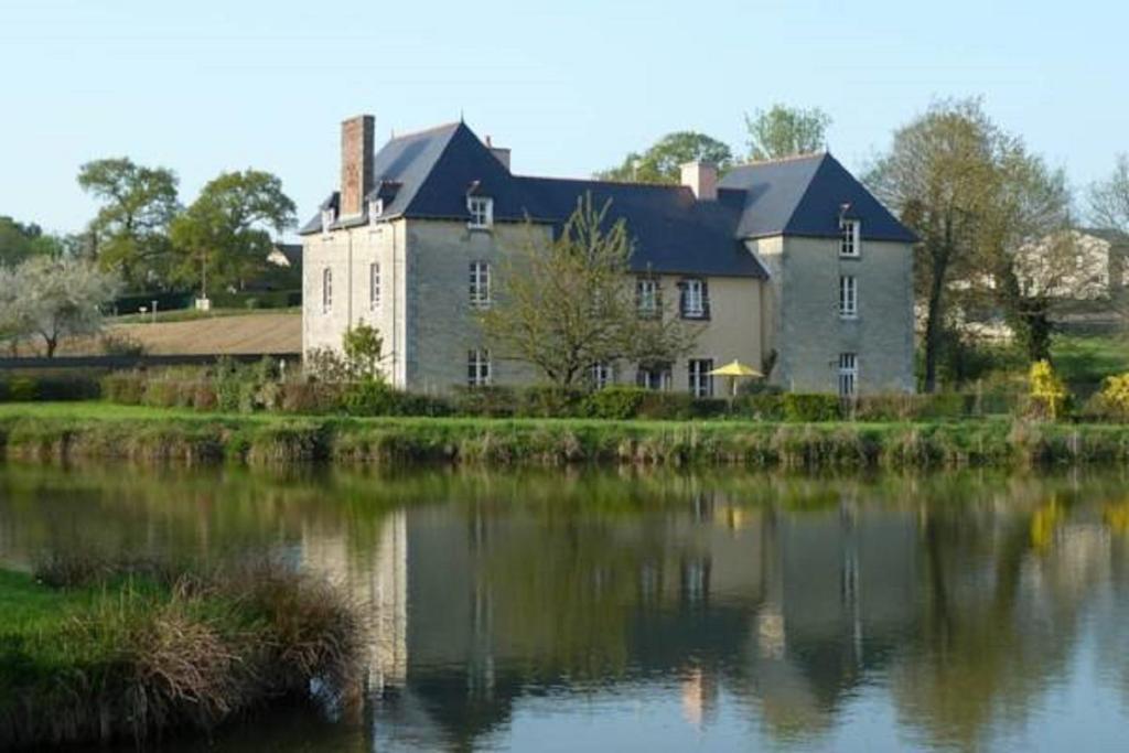 una casa grande sentada junto a un cuerpo de agua en B&B L'Atelier du Presbytère, en Saint-Maugan