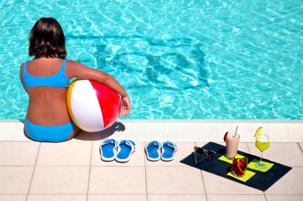 una mujer sentada junto a una piscina con una pelota de playa y zapatos en Kora Park Resort, en Formia