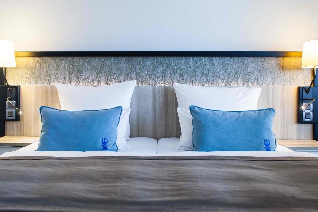 a large bed with two blue pillows on it at Hotel Neptun in Warnemünde