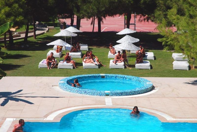 a group of people sitting around a swimming pool at Hotel Flora Suites - All Inclusive in Kuşadası