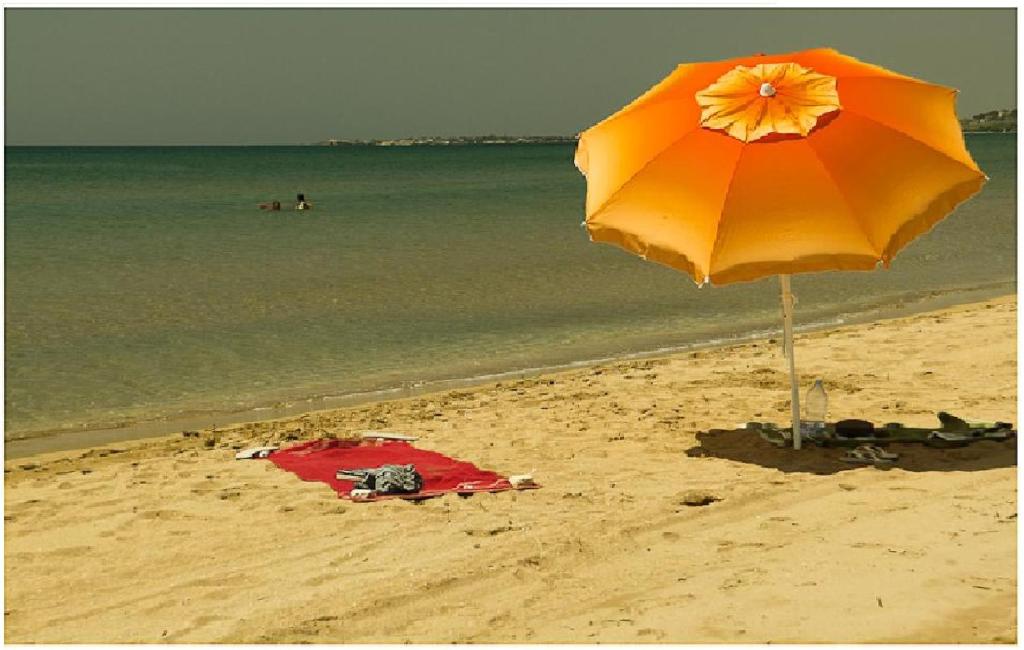 an orange umbrella on a beach with the ocean at camping Venere in Granelli