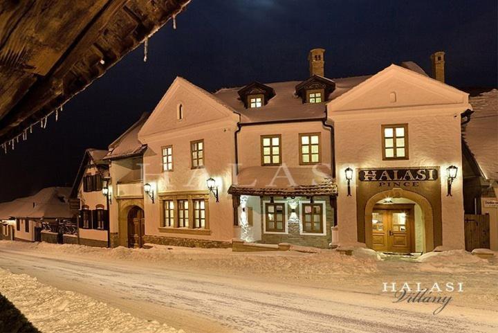 a large building on a snowy street at night at Halasi Pince Panzió in Villány
