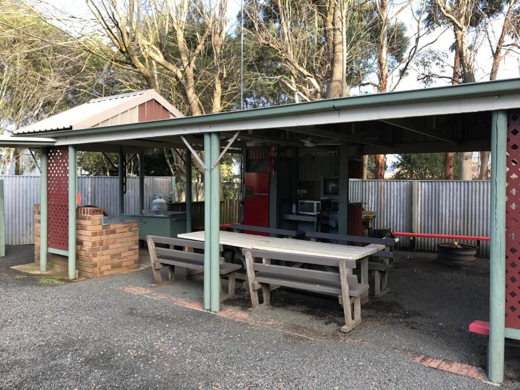 a picnic table and benches under a shed at Pinewood Caravan Park in Heywood
