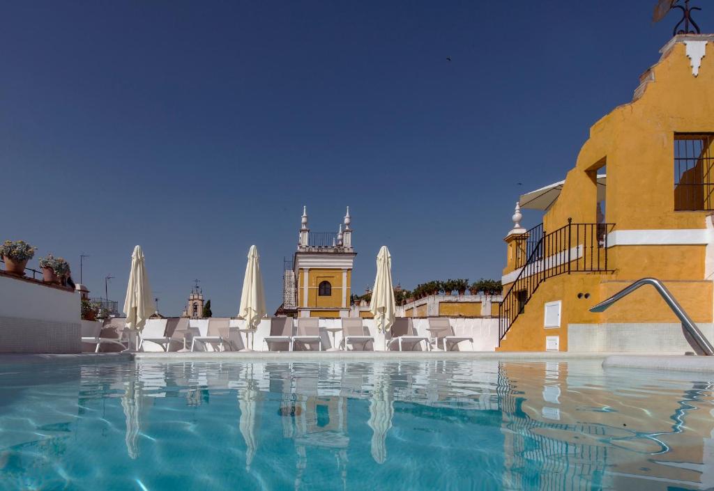 uma piscina com cadeiras brancas e um edifício em Hotel Las Casas de la Judería em Sevilha