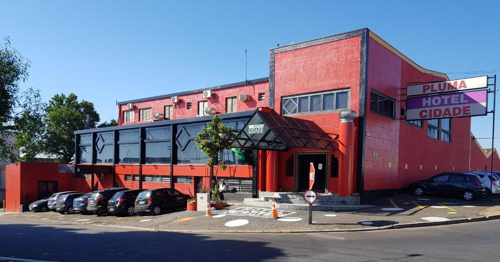 un edificio rojo con coches estacionados en un estacionamiento en Pluma Hotel Cidade, en Americana