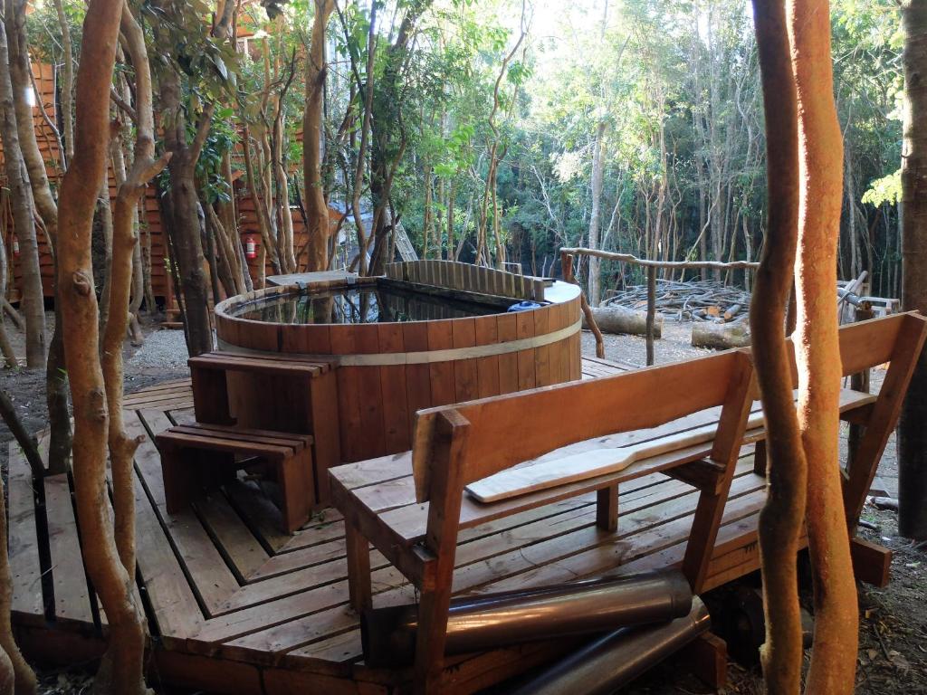 una terraza de madera con bañera de hidromasaje y 2 bancos en Cabañas Ensenada Bosque Nativo, en La Ensenada