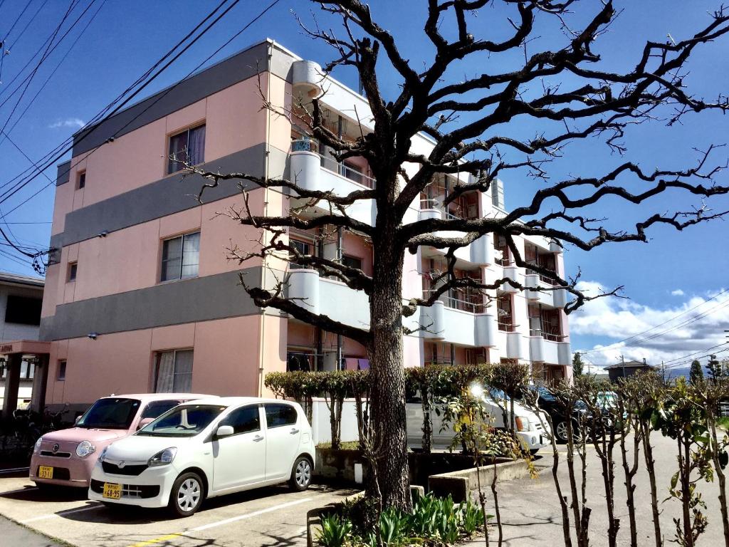 een witte auto geparkeerd voor een roze gebouw bij Backpackers Dorms Miwa Apartment in Nagano