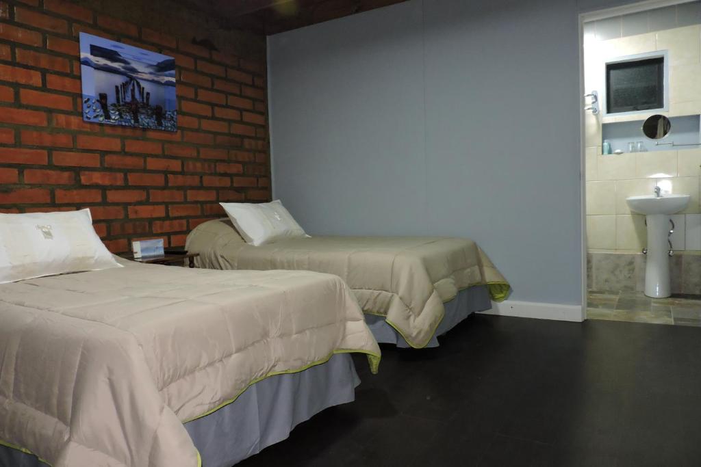 a room with two beds and a sink and a brick wall at Maromava Patagonia in Puerto Natales