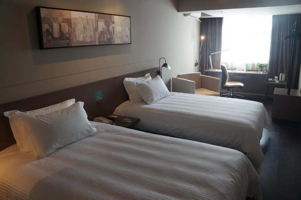 a hotel room with two beds and a chair at Jinjiang Inn Haikou Guomao Jinlong Road in Haikou