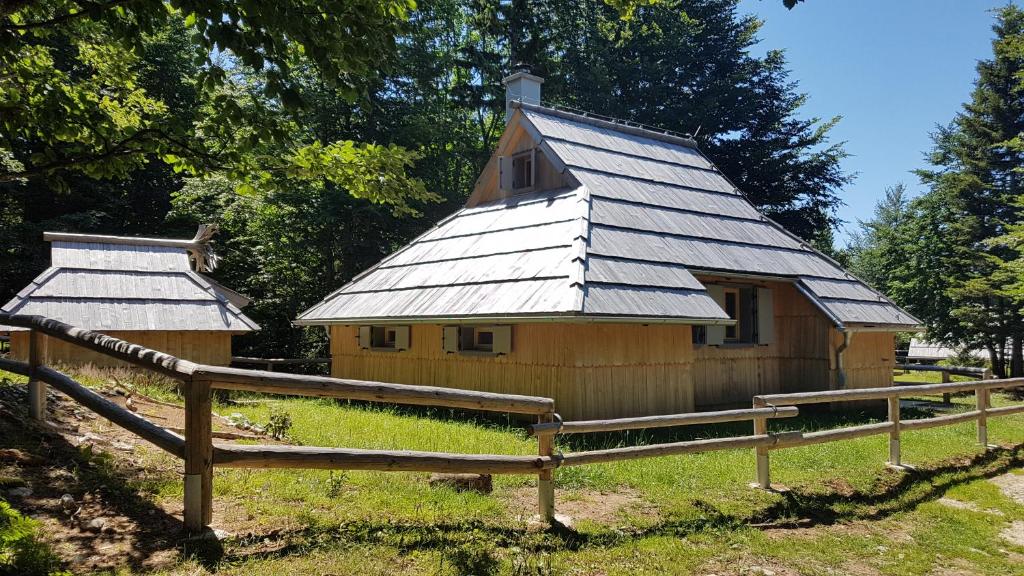 ein Holzgebäude mit einem Metalldach neben einem Zaun in der Unterkunft Koča Predilnica Velika Planina in Kamniška Bistrica