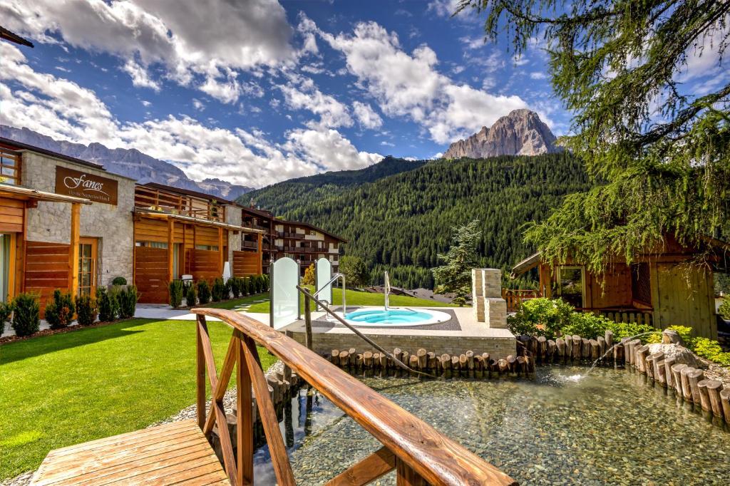 a resort with a bridge over a pool and mountains at Hotel Fanes in Selva di Val Gardena