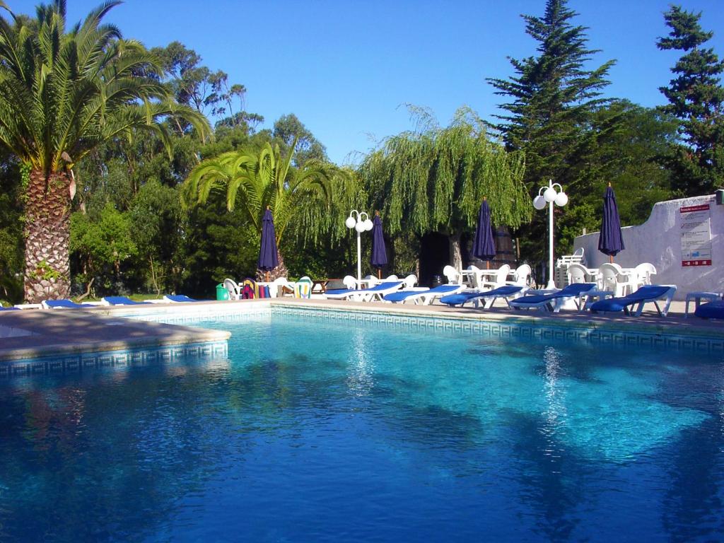 a large swimming pool with chairs and umbrellas at Hotel Rural A Coutada in Atouguia da Baleia