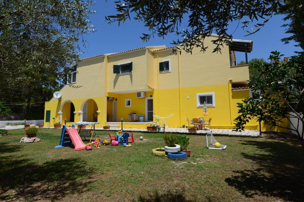 una casa gialla con bambini che giocano in cortile di Roula's Studios & Apartment ad Acharavi