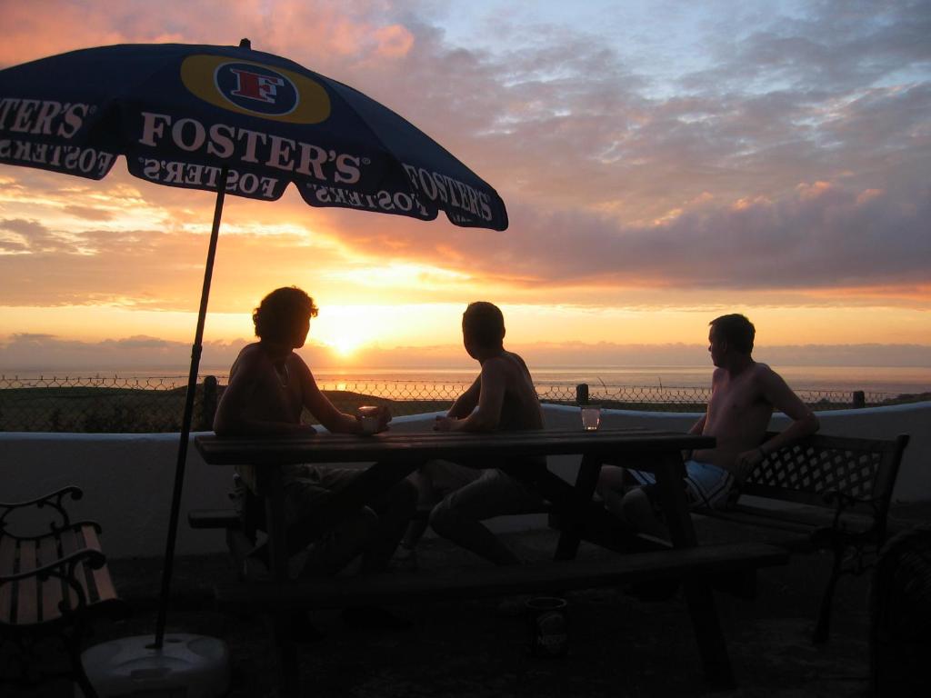 three men sitting at a table under an umbrella at Longbeach- Adults Only in Newquay