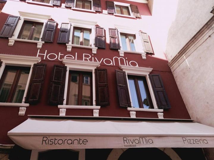 ein rotes Gebäude mit einer weißen Markise davor in der Unterkunft Hotel RivaMia in Riva del Garda