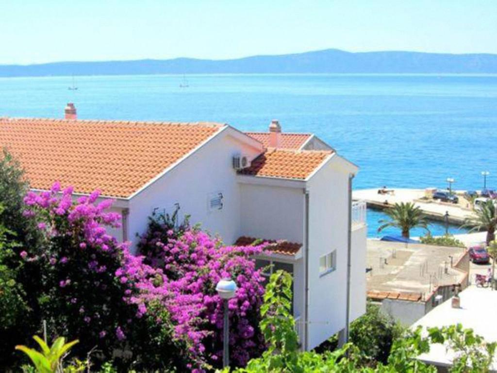 a building with purple flowers in front of the ocean at Luka Kokić Apartments in Podgora