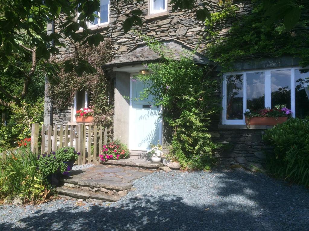 a stone house with a white door and flowers at Stockghyll Cottage in Bowness-on-Windermere