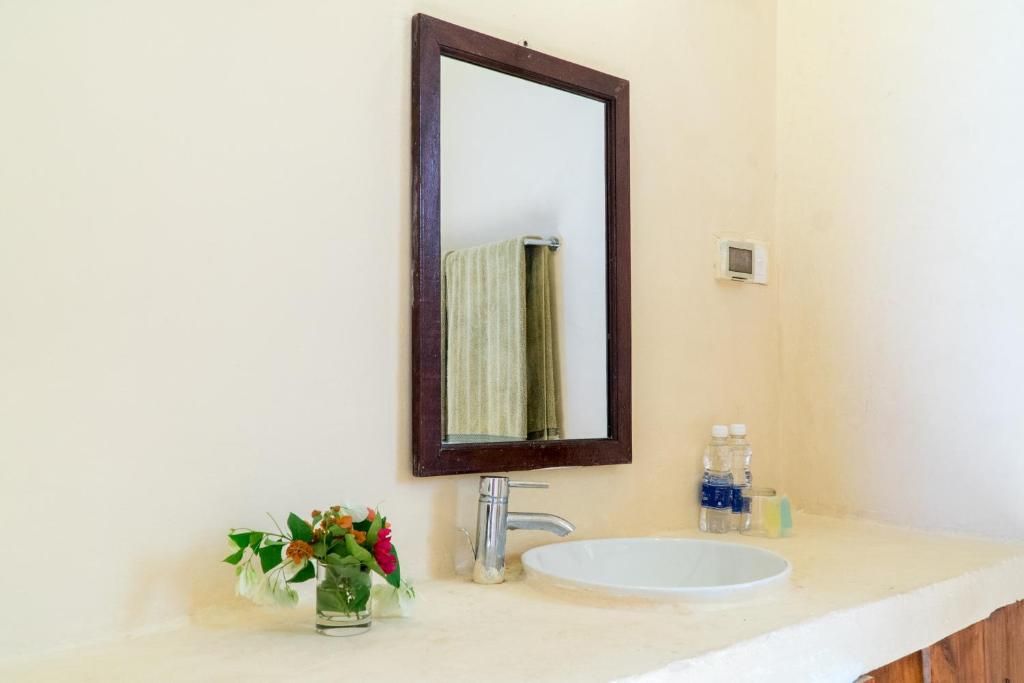 um lavatório de casa de banho com um espelho e um vaso de flores em Cristal Resort em Paje