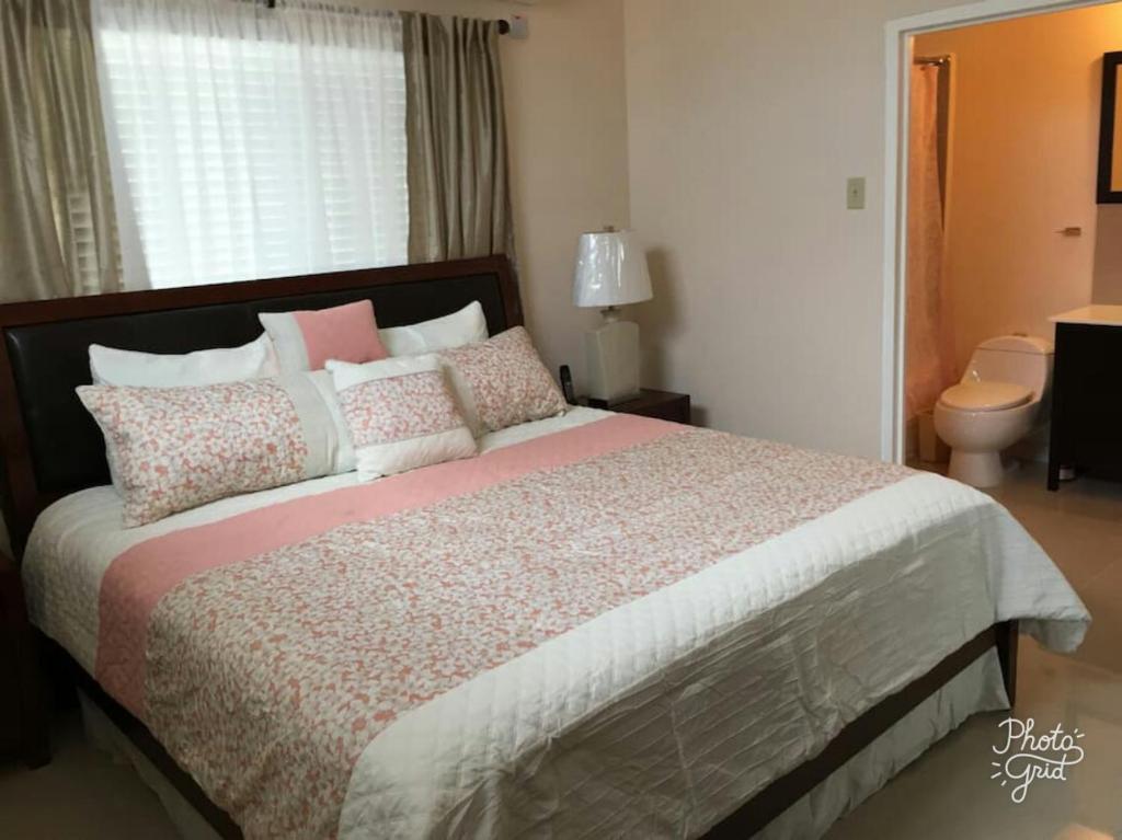 Spanish TownにあるCaymanas Estate beautiful three bedroom houseのベッドルーム1室(ピンクと白の枕が備わる大型ベッド1台付)