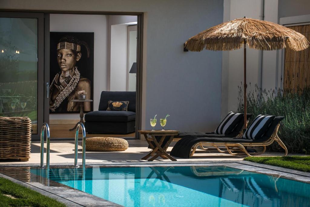 einem Pool mit Stühlen und einem Sonnenschirm neben einem Haus in der Unterkunft Sunvillage Malia Boutique Hotel and Suites in Malia