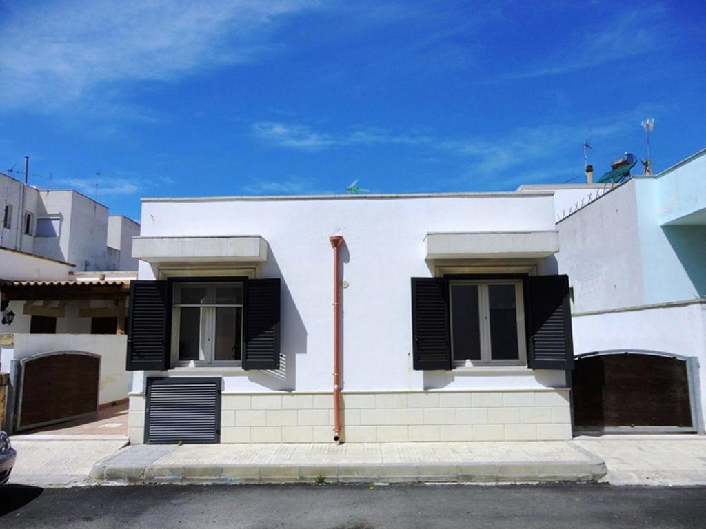 une maison blanche avec volets noirs dans une rue dans l'établissement Appartamenti Carneo Torre San Giovanni - Verso sud, à Torre San Giovanni