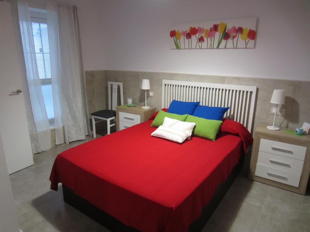 Un dormitorio con una cama roja con almohadas azules y verdes en Botic4, en Cádiz
