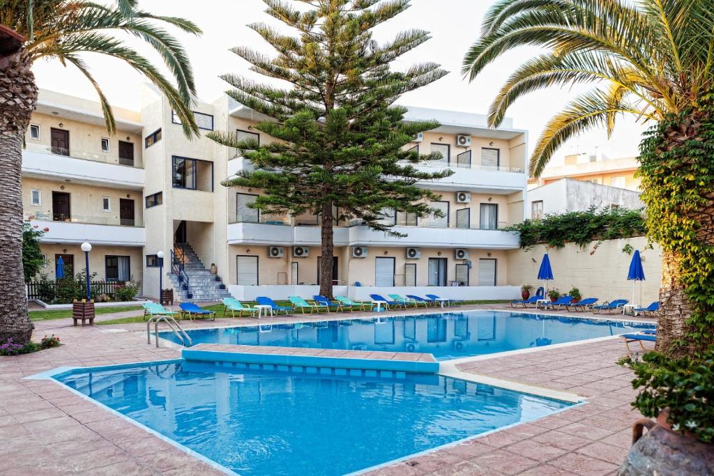 a swimming pool in front of a hotel with palm trees at Cretan Sun in Platanes