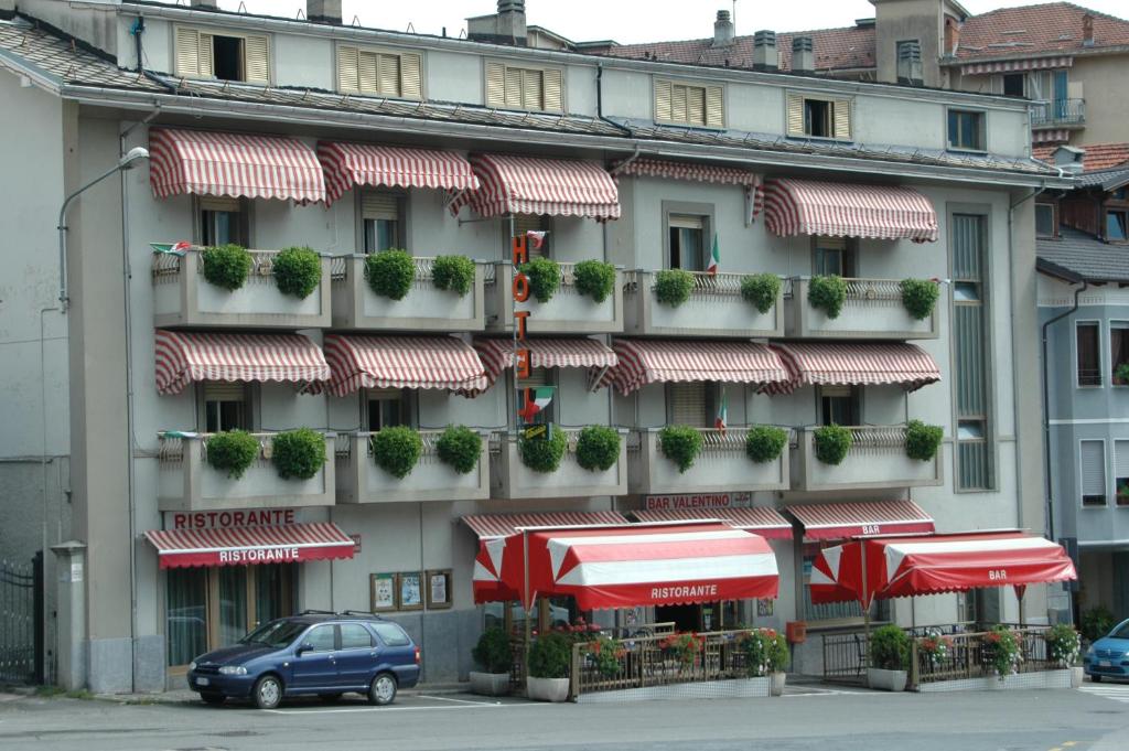 ein Gebäude mit roten und weißen Sonnenschirmen davor in der Unterkunft Hotel Valentino in Perosa Argentina