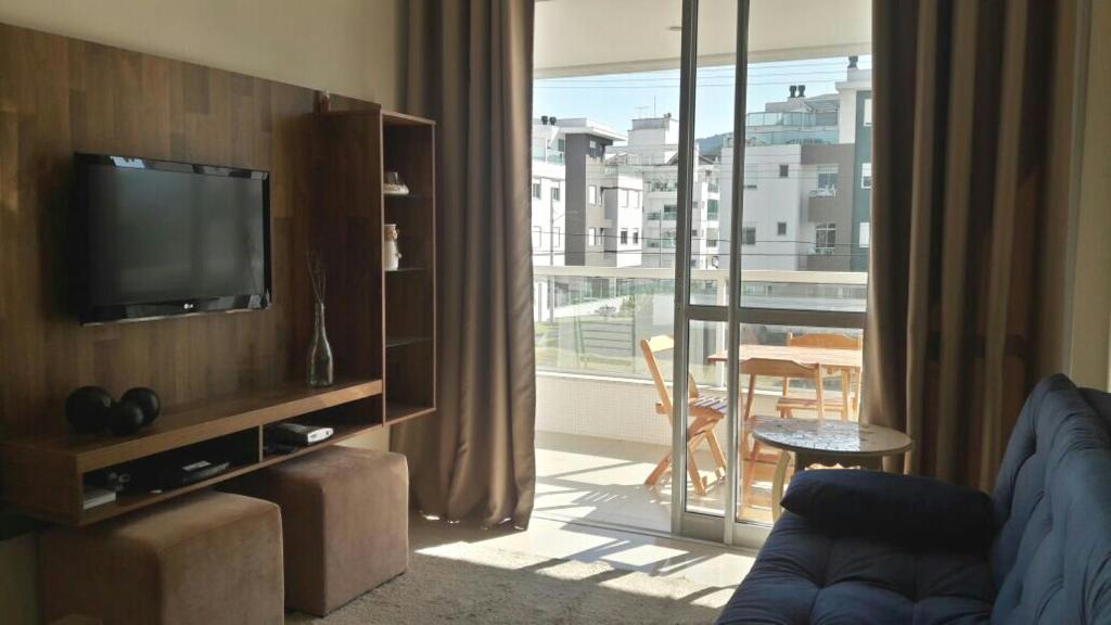 een woonkamer met een bank, een tv en een balkon bij Residencial Encantos do Mar in Florianópolis